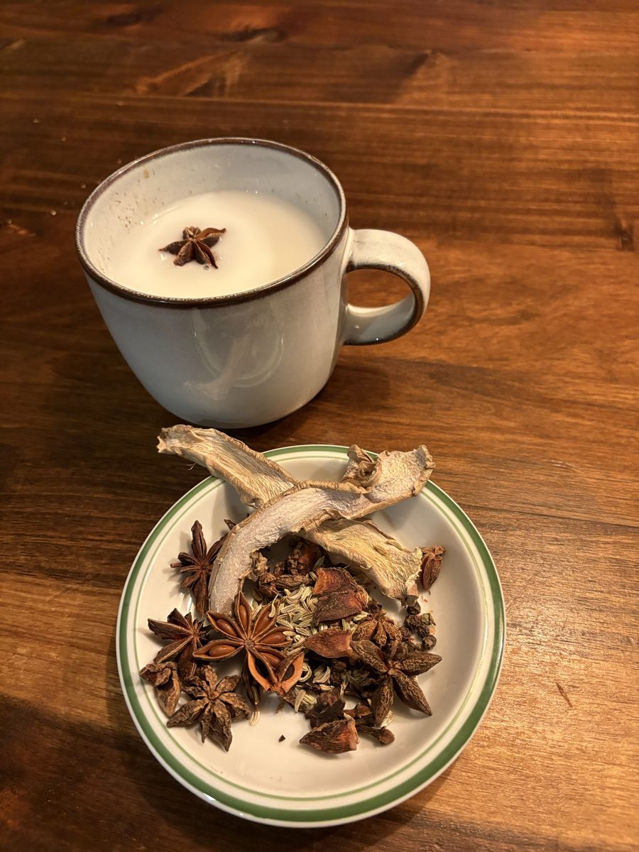 Chávena de chai com leite e anis-estrelado, ao lado de um pires com especiarias secas